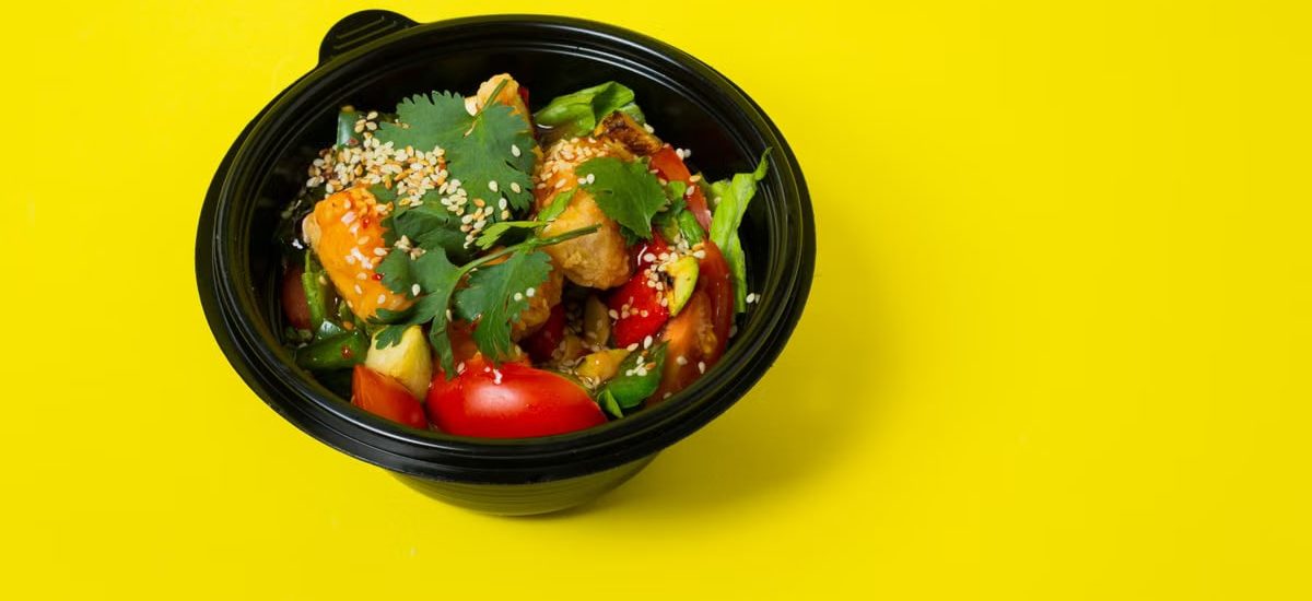 From above of delicious healthy salad consisting of various vegetables in plastic bowl placed on bright yellow background
