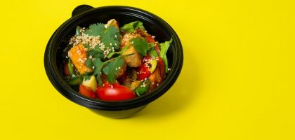 From above of delicious healthy salad consisting of various vegetables in plastic bowl placed on bright yellow background