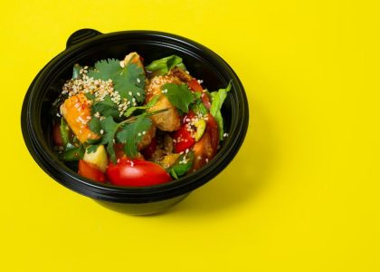 From above of delicious healthy salad consisting of various vegetables in plastic bowl placed on bright yellow background