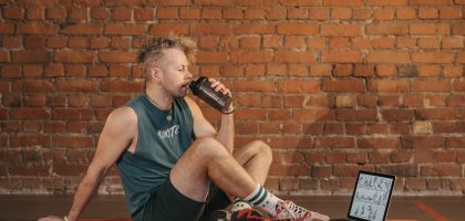 Athletic man sitting on exercise mat with water bottle, taking a break from workout, in a rustic indoor setting.