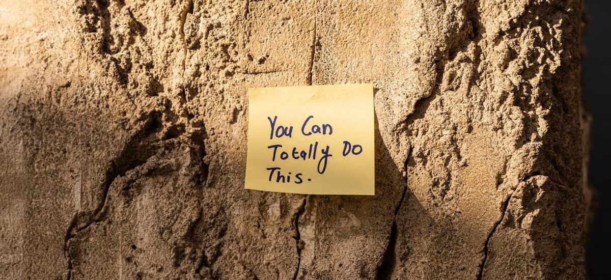 A sticky note with a motivational message on a textured wall in Dubai, with sunlight casting shadows.