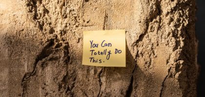 A sticky note with a motivational message on a textured wall in Dubai, with sunlight casting shadows.