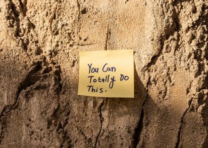 A sticky note with a motivational message on a textured wall in Dubai, with sunlight casting shadows.